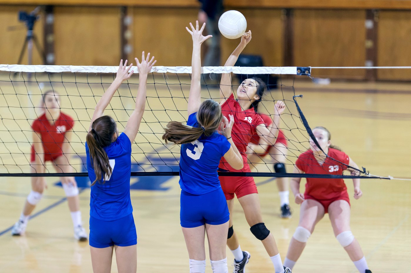 Asian high school volleyball player spikes volleyball against female opponents